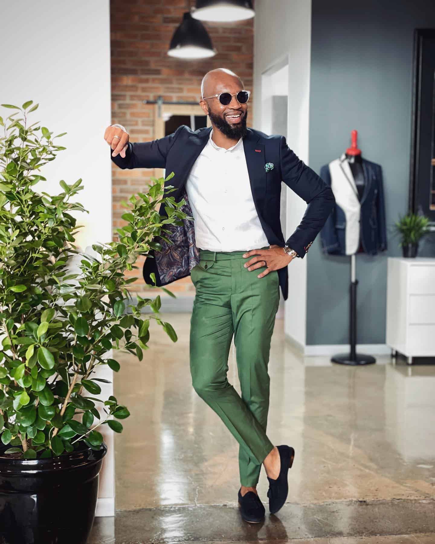 bald man standing cross legged wearing blue blazer and green pants