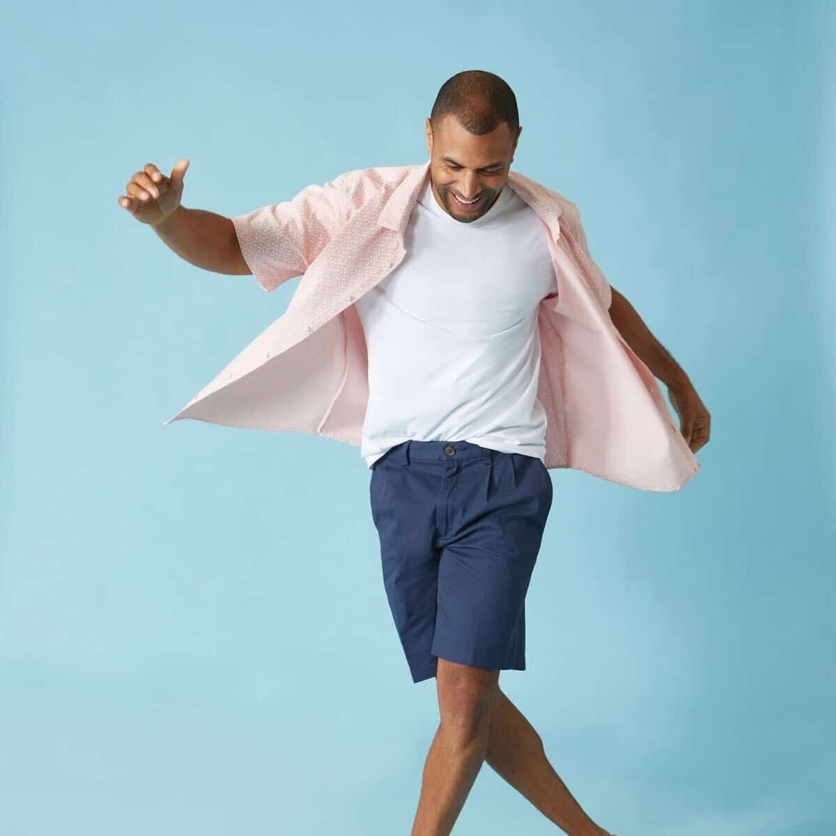 man in pink shirt and navy pleated shorts