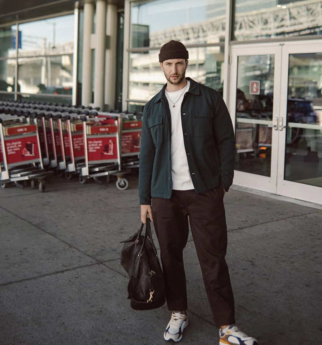 Man standing outside of a Airport, holding a duffle bag