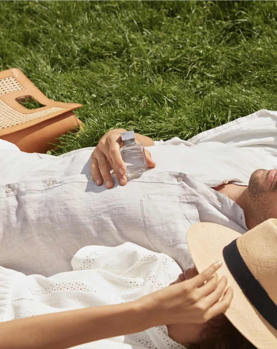 Man lying in the grass with a cologne bottle on his chest showing how to wear cologne in the summer heat