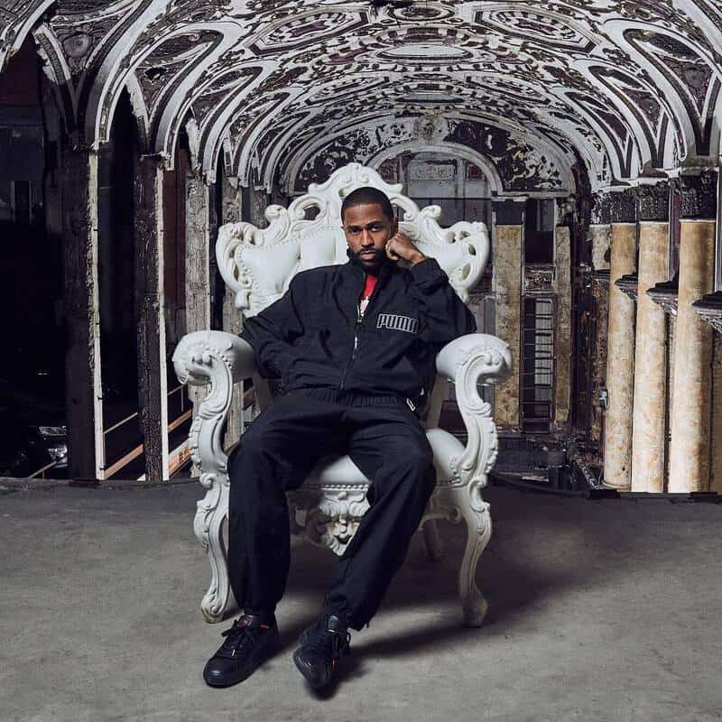 man sitting on a white chair wearing an all black outfit by puma