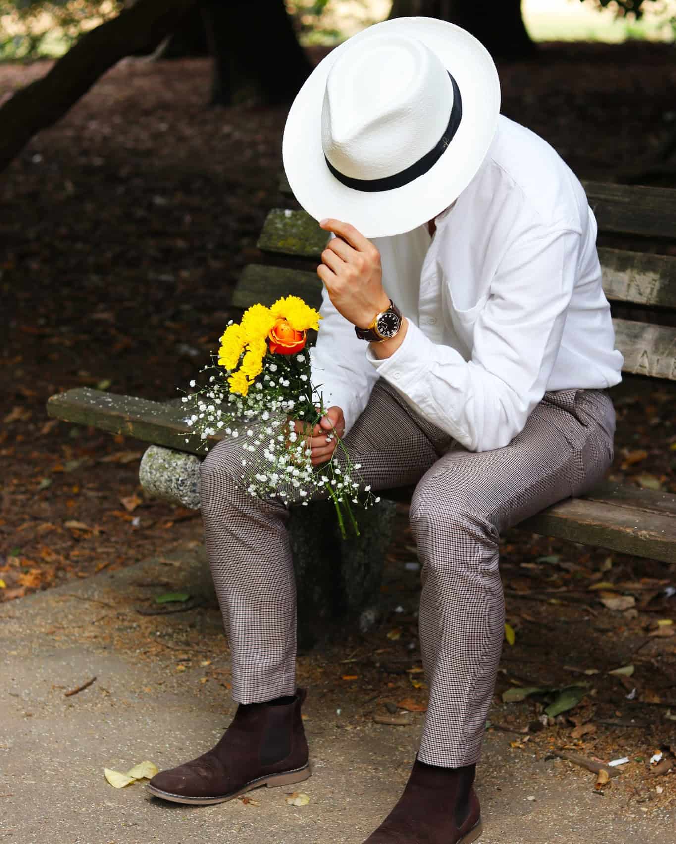 man in a panama hat sitting on a bench holding a bunch of flowers