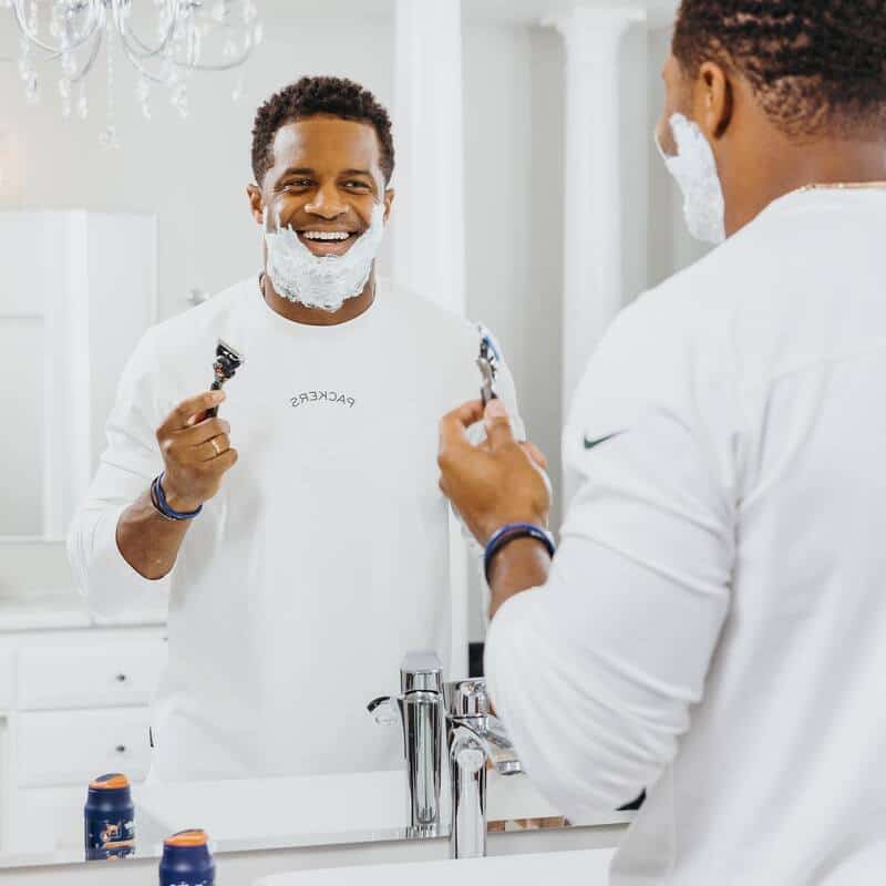 man with shaving cream on face smiling at his face in the mirror