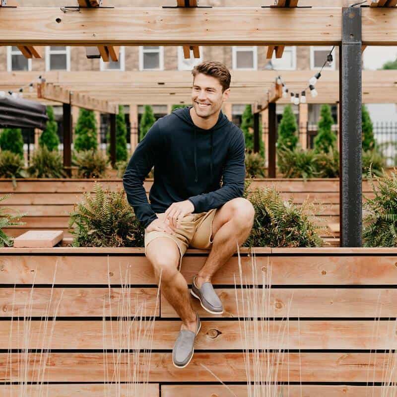 man sitting on a wooden fence wearing a hoodie and shorts