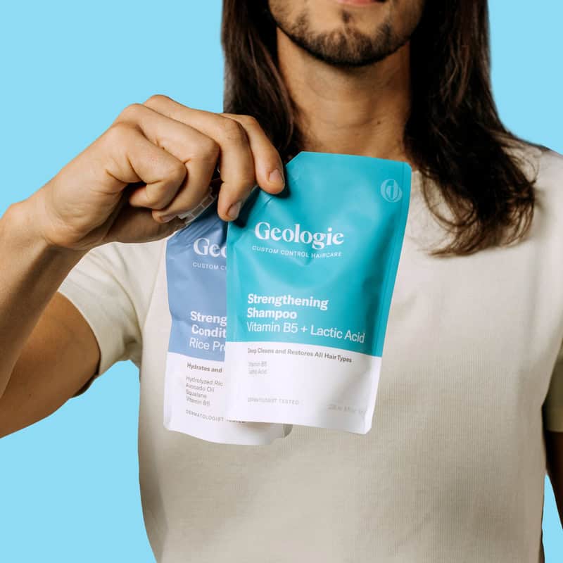 man with long hair holding a Geologie Shampoo and Conditioner