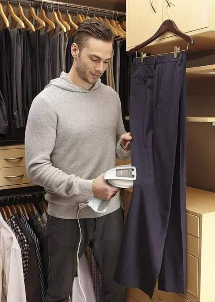 man using a Hanheld garment steamer to straighten the pants