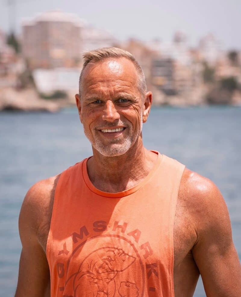 a physically fit man with short grey hair wearing an orange tank top