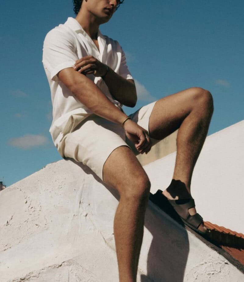 man sitting on the roof wearing a short sleeved shirt and shorts
