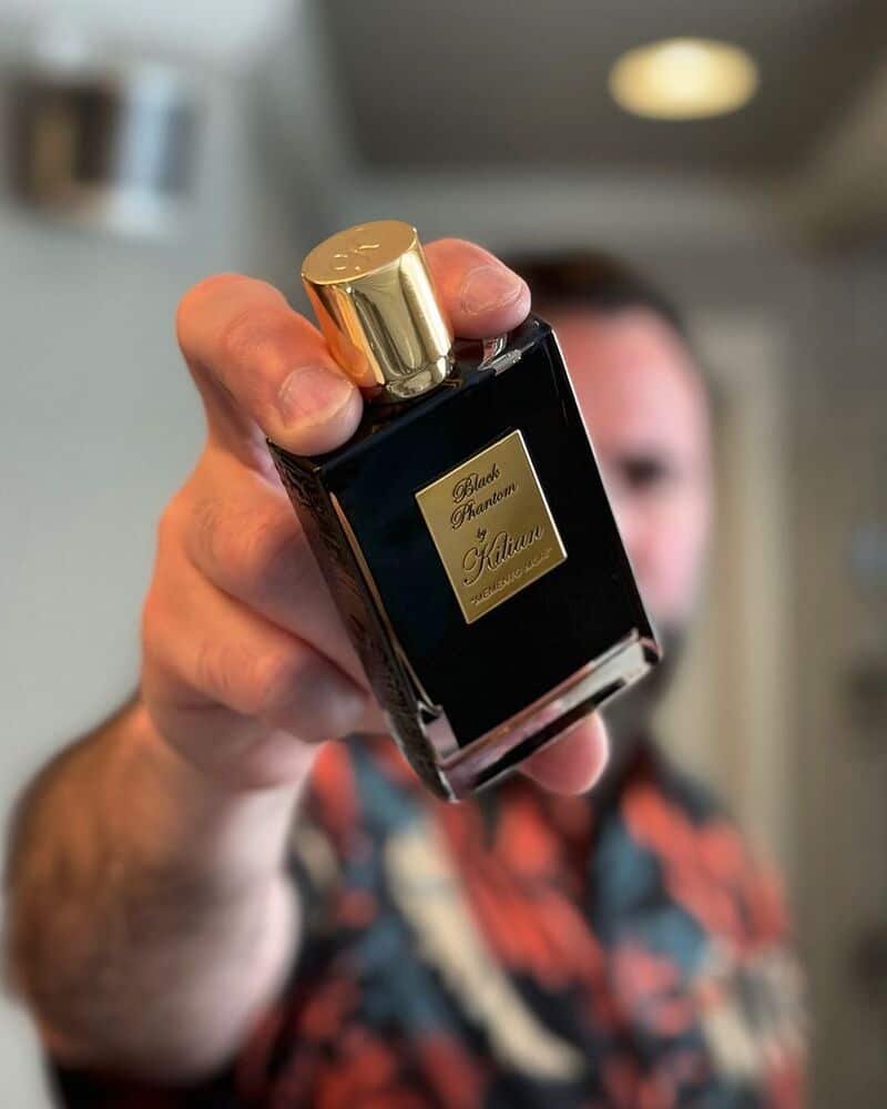 A man holding a bottle of Black Phantom Cologne by Kilian