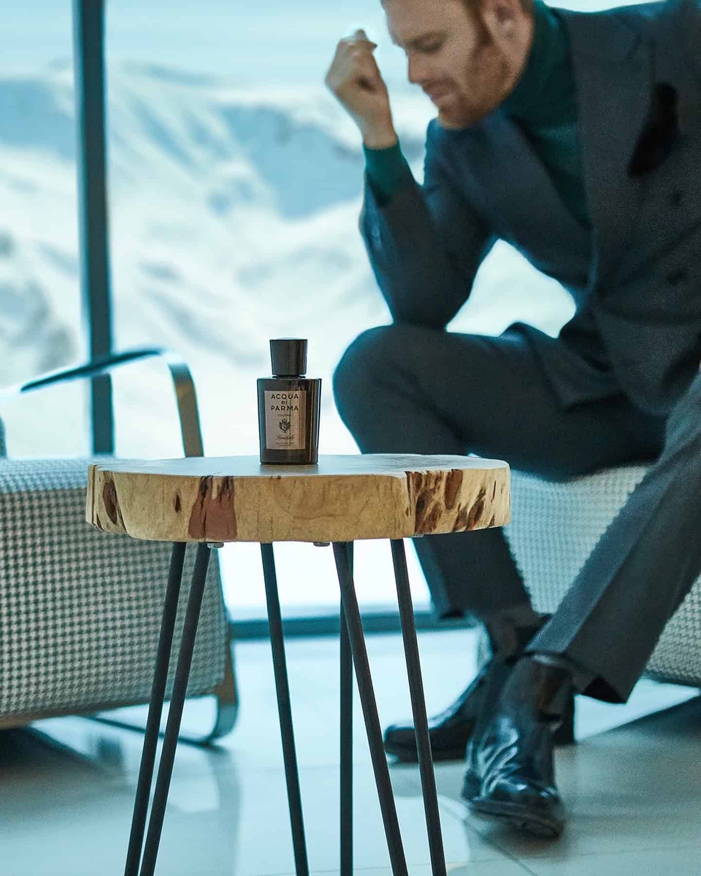 man sitting on a chair and a bottle of Acqua Di Parma Cologne