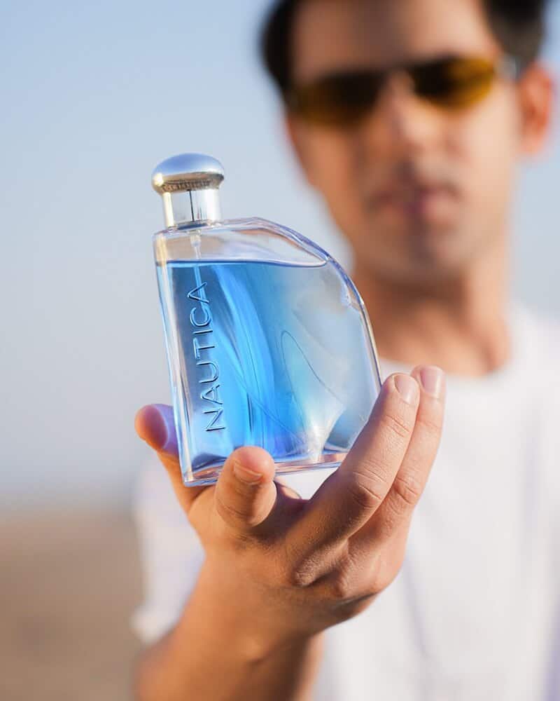 a man holding a bottle of nautica blue cologne