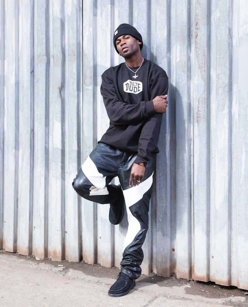 man with black sweater and beanie leaning to a metal fence