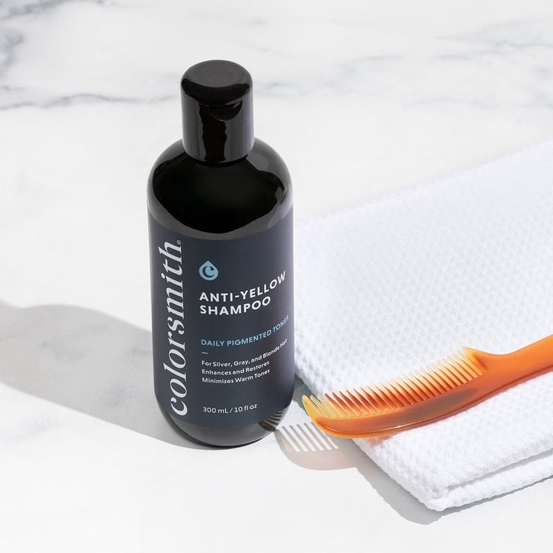 A bottle of Color Smith anti-yellow shampoo with a towel and comb on the side