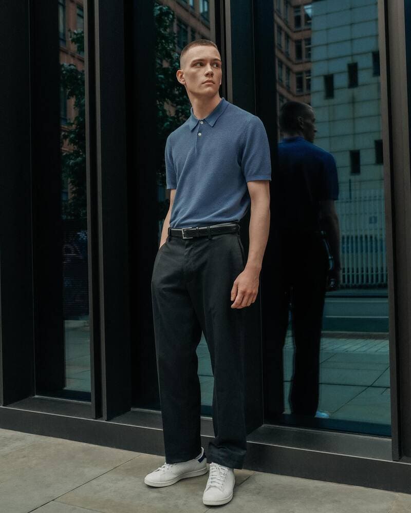 man standing by the building wearing a navy polo shirt and black pants