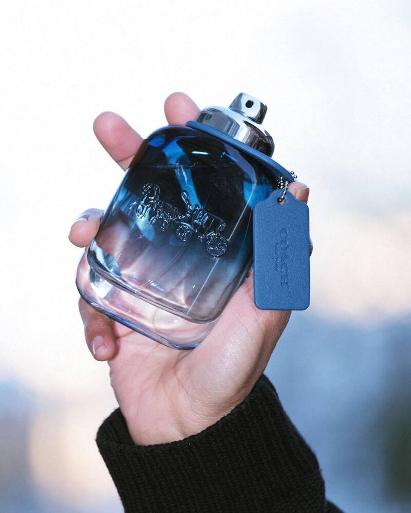 holding a bottle of Coach Blue Cologne