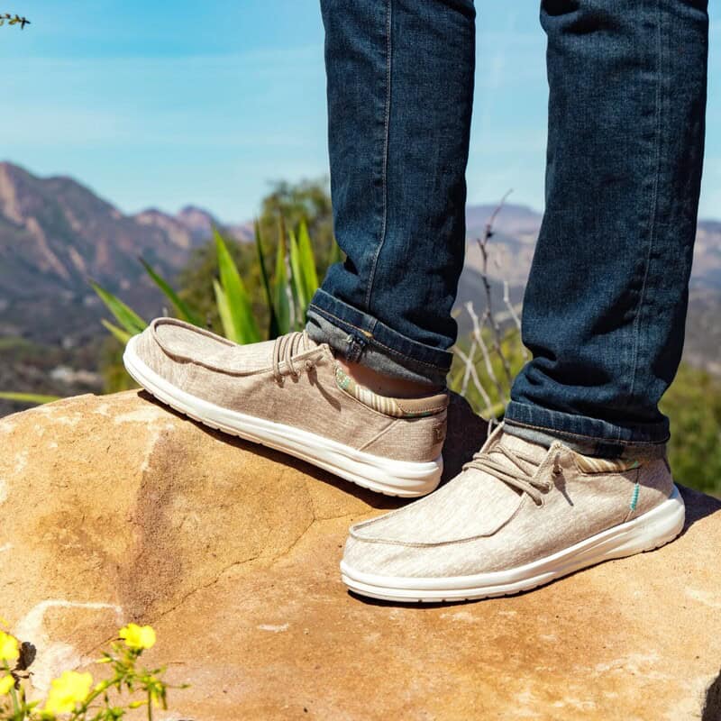 man standing on a big rock and wearing a pair of hey dude shoes