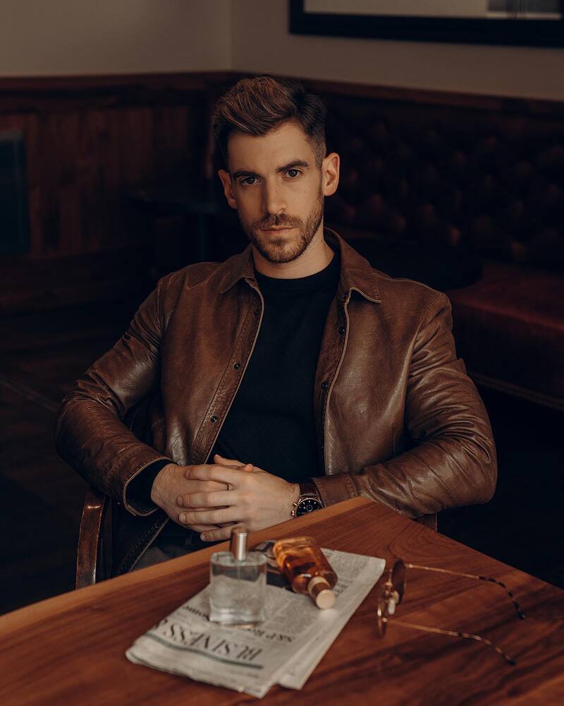 bottles of Spirit and Original Stetson colognes on the table and a man wearing a leather jacket sitting on a chair