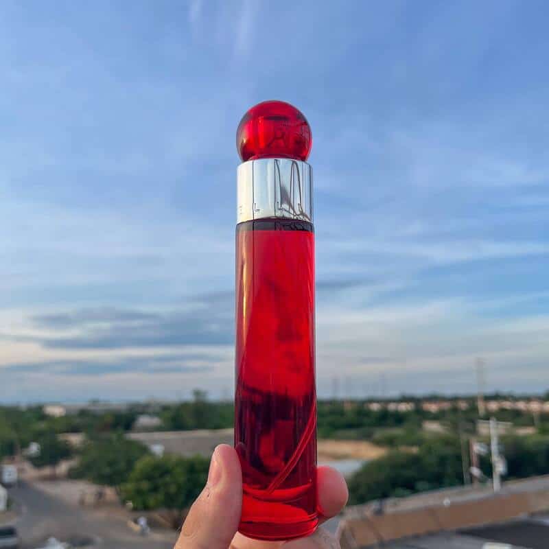 A man holding a bottle of perry ellis 360 red cologne