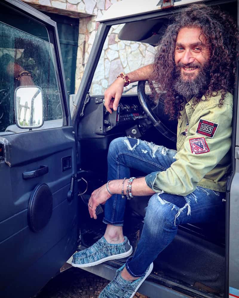 man with long curly hair sittin in the drivers seat with door open