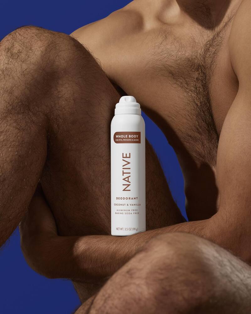 A bottle of Native Deodorant body spray with a body of a man as background