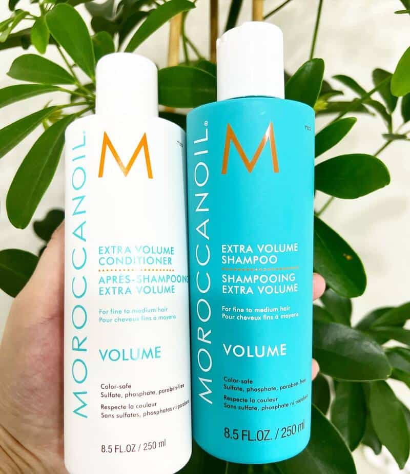holding a bottle of Extra Volume conditioner and Shampoo by Moroccanoil