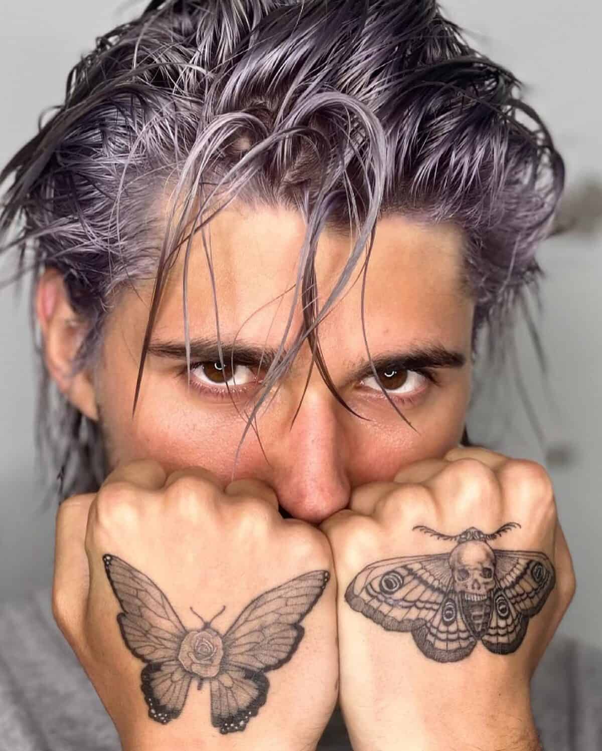 man with butterfly and moth tattoo on the back of his hands