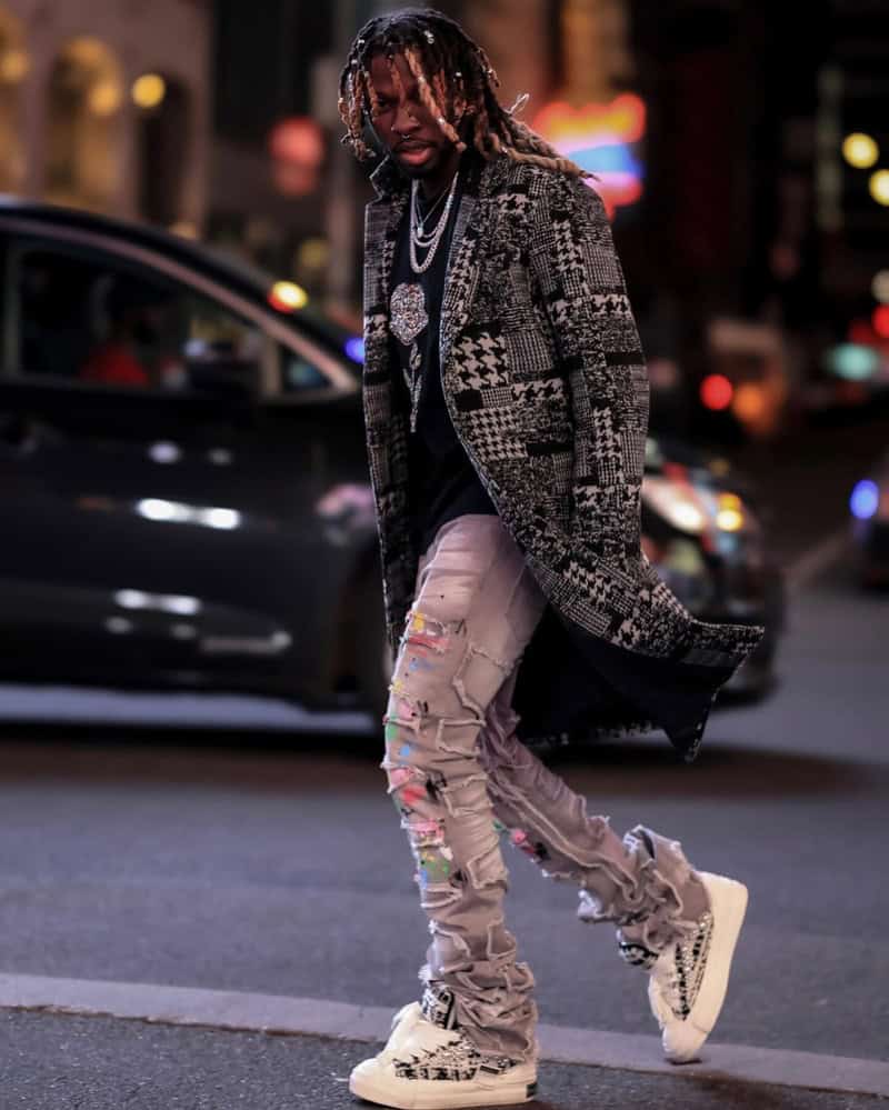 man crossing the street wearing a checked long coat and stacked jeans