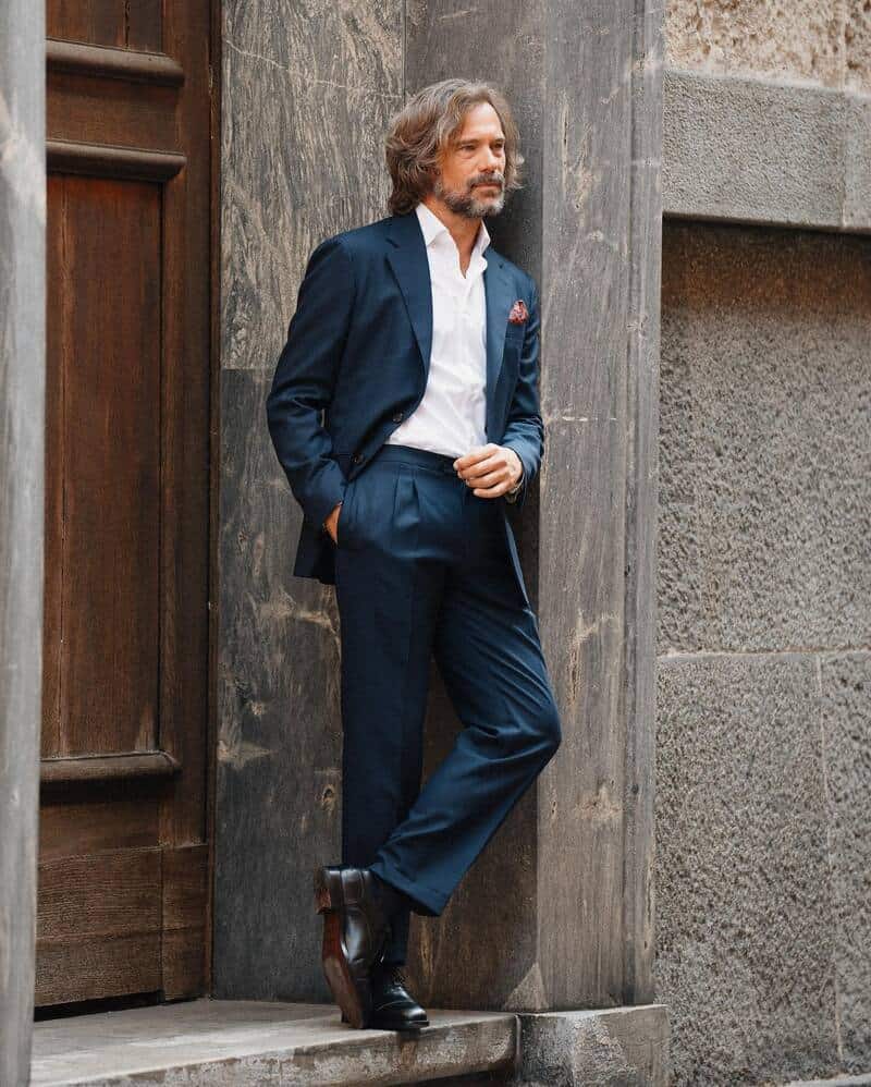man in a navy suit leaning to a wall of a building