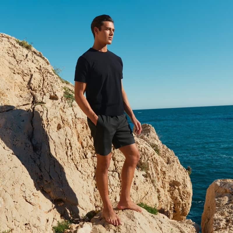 man in a black t-shirt and shorts standing on a cliff