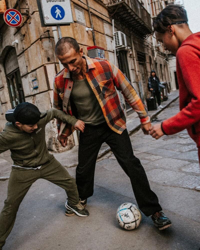man playing football in the street with the kids