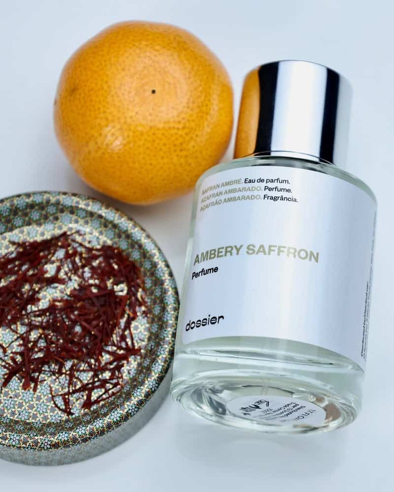 a bottle of Ambery Saffron Perfume by Dossier with saffron spice and a grapefruit on the side