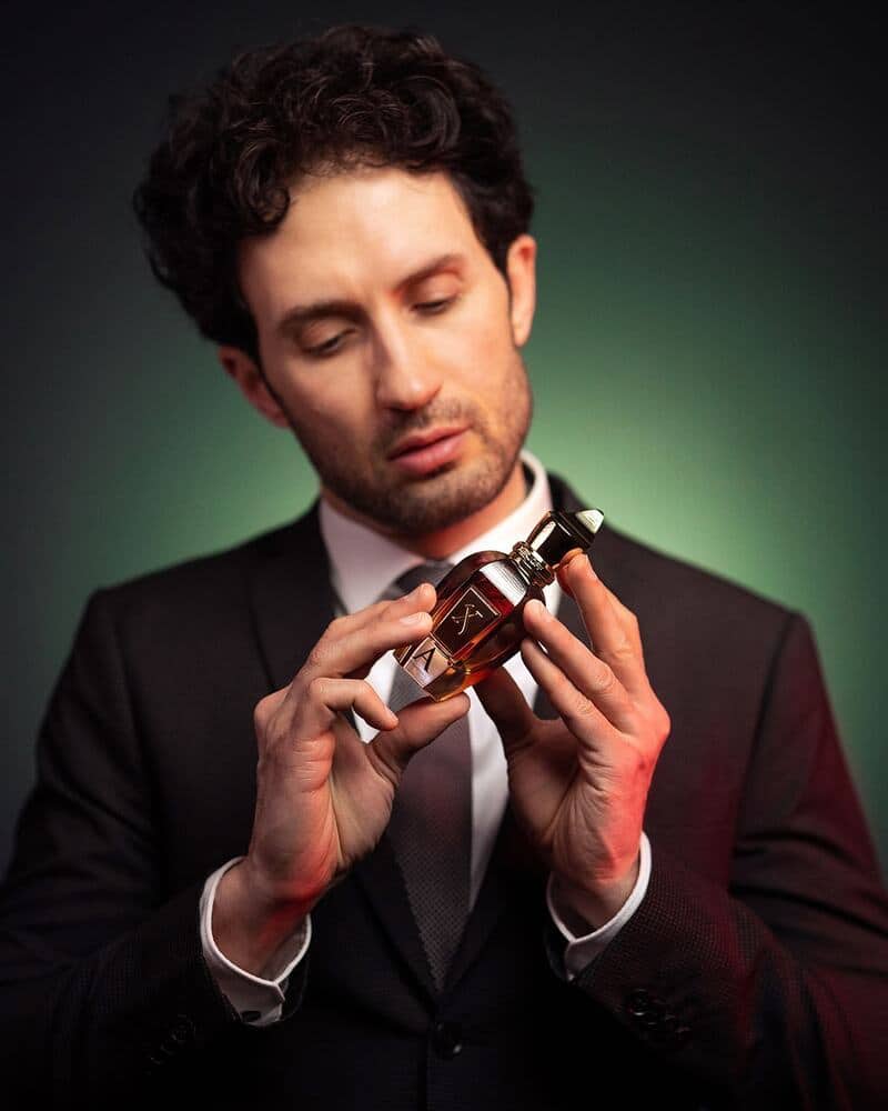 man in suit holding a bottle of alexandria II by Xerjoff