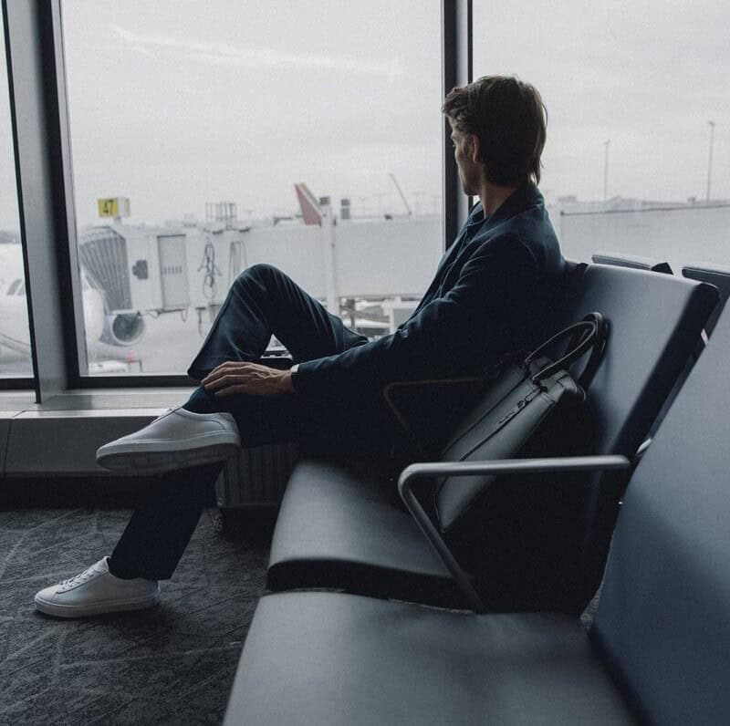 man sitting at the airport wearing a pair of white sneakers by KOIO