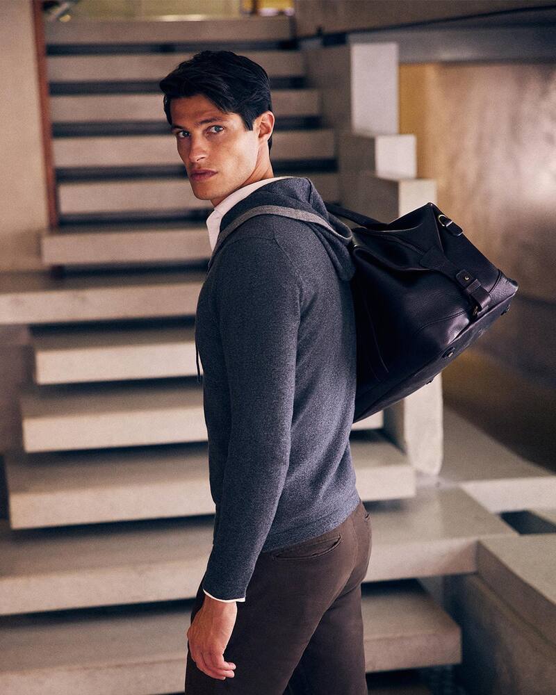 man wearing a luca faloni zip-hoodie and carrying a weekender bag