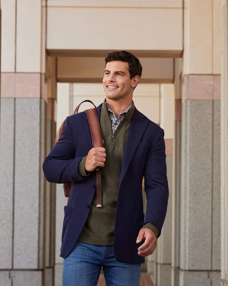 man in a navy blazer and jeans carrying a backpack