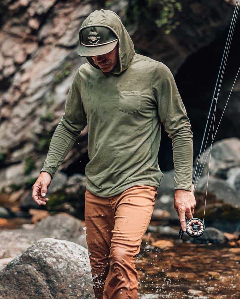 man wearing a hoodie by poncho outdoors and holding a fishing rod