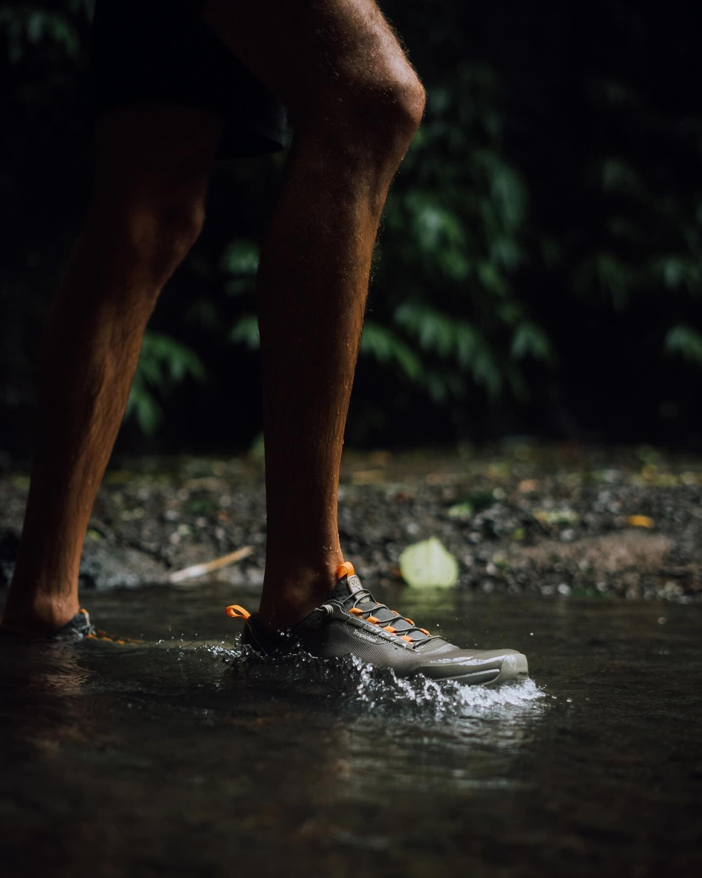 man wearing a pair of All Terrain Sneakers by Tropicfeel while walking in a stream