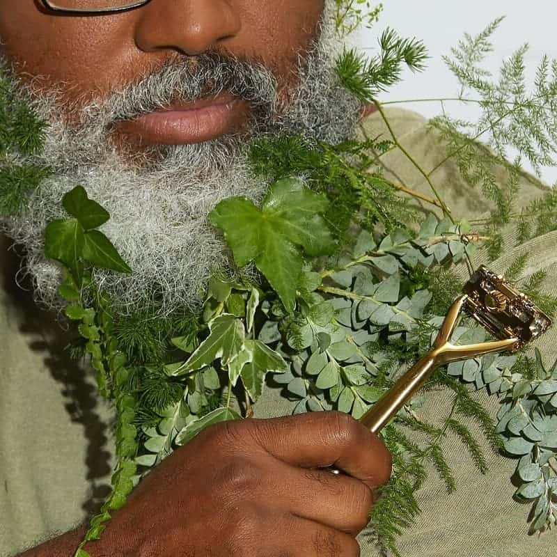 man with leaves in his beard while holding a gold razor by Leaf Shave