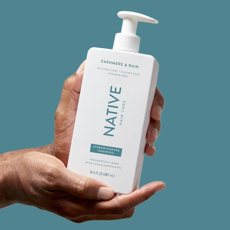 holding a bottle of Cashmere and Rain Strengthening Shampoo by Native