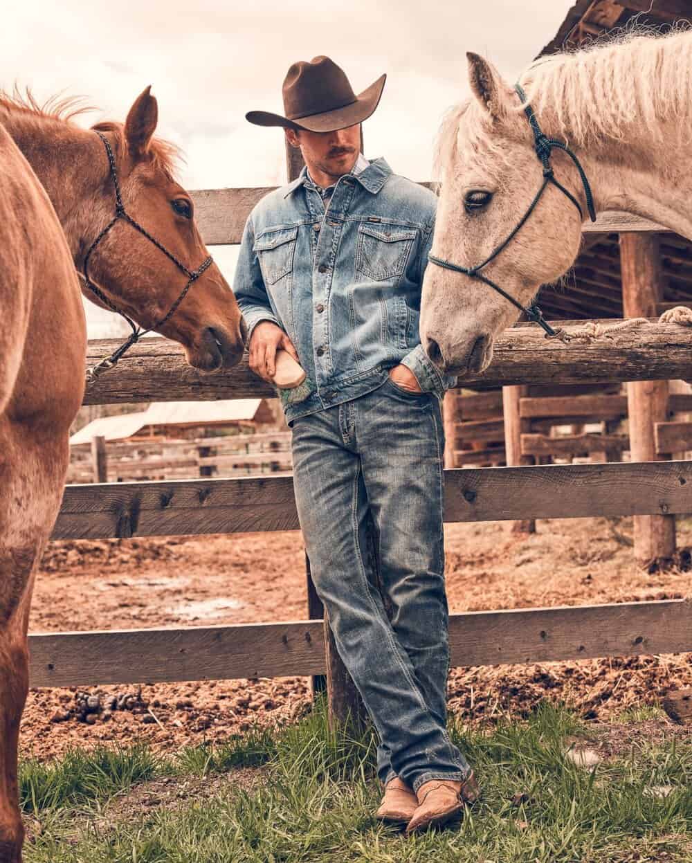 a cowboy leaning to a wooden fence and two horses