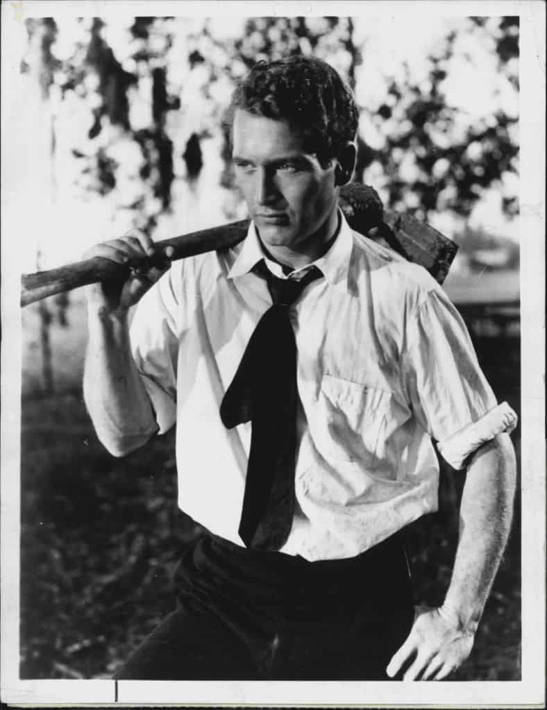 Paul Newman in a shirt rolled up to the elbows while carrying a pick axe on his shoulder