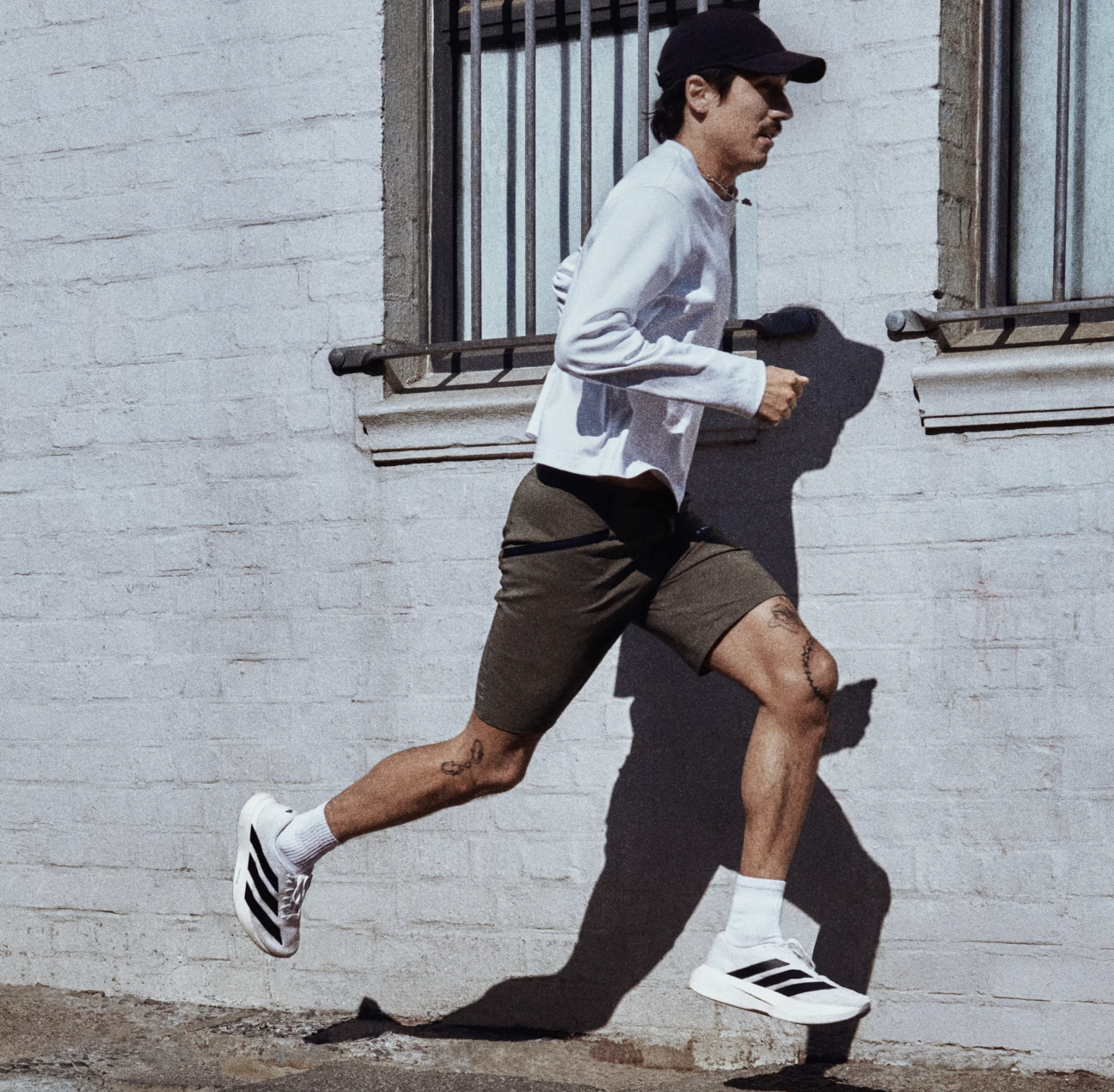 Running man in casual athletic outfit with shorts, white jacket, and sneakers on a city sidewalk, capturing urban fitness and streetwear style for men's sportswear and lifestyle fashion.