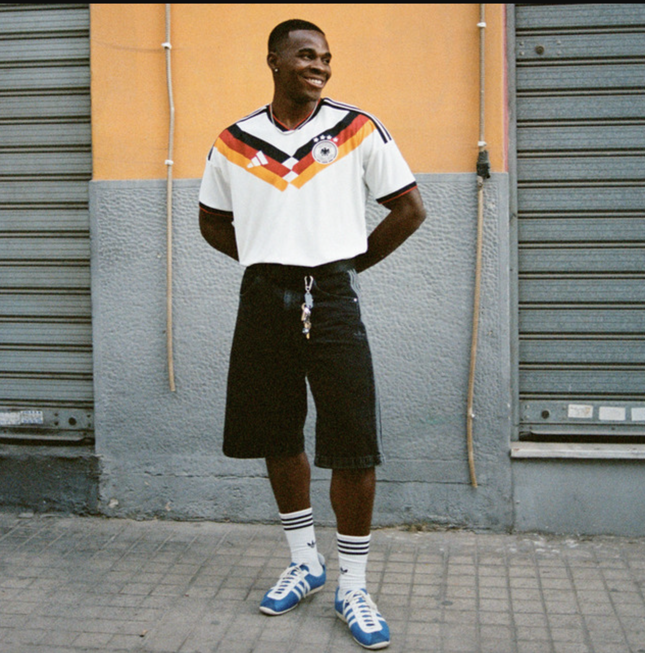 Men's casual streetwear style featuring a vintage soccer jersey with black shorts, Adidas sneakers, and Moody's signature casual vibe, perfect for urban fashion and sports-inspired looks.